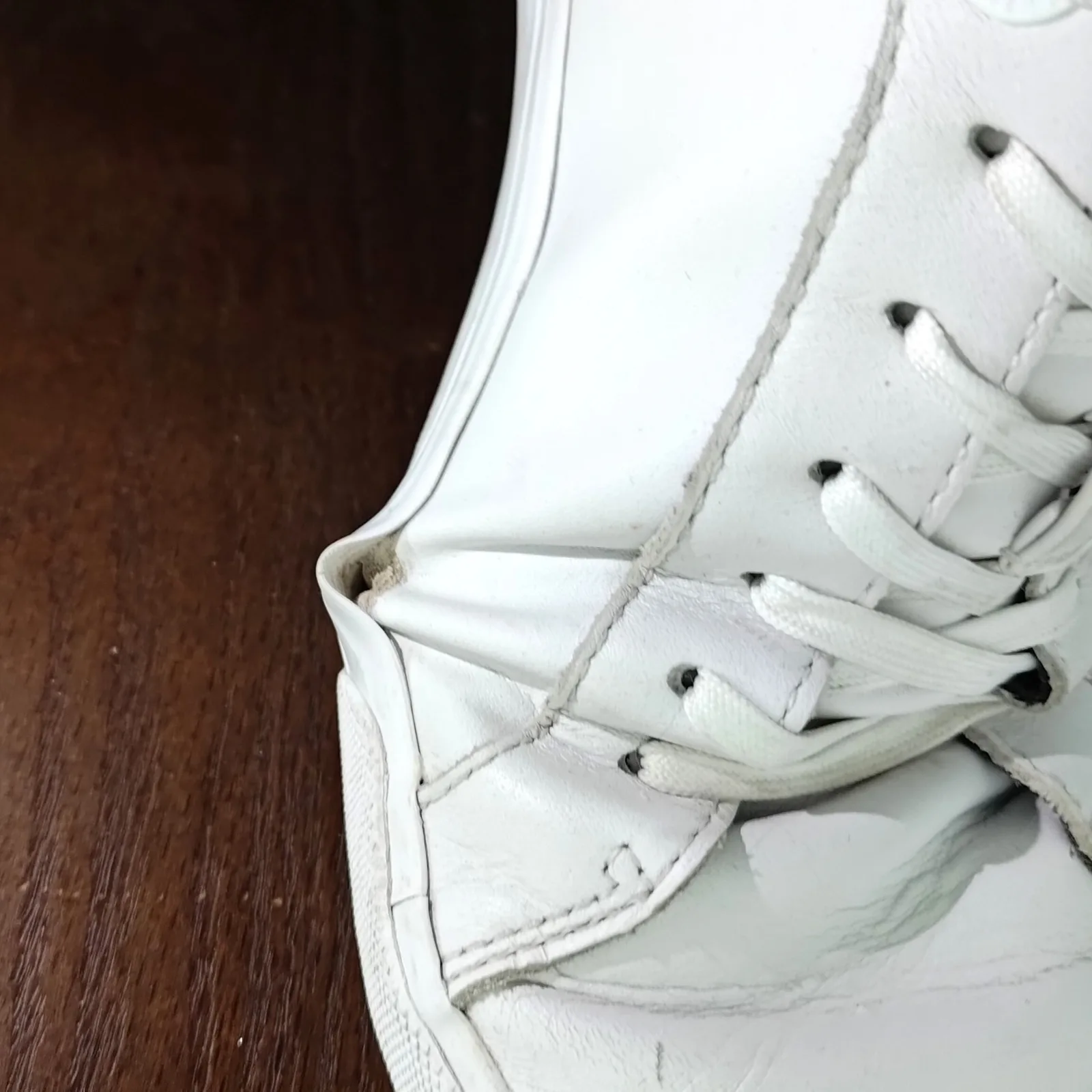 Ferse eines weissen Ledersneakers, die Sohle löst sich vom Schaft